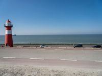 a red and white lighthouse with blue sky near a road and car on it's side