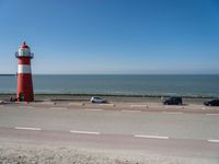 a red and white lighthouse with blue sky near a road and car on it's side