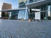 there is a black bench in the middle of a brick plaza with two buildings behind it