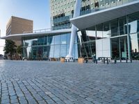 there is a black bench in the middle of a brick plaza with two buildings behind it