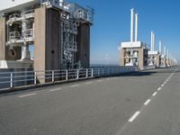 the view of a bridge with pipes and stairs in front of it, and buildings to the side of it