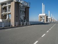 the view of a bridge with pipes and stairs in front of it, and buildings to the side of it