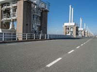 the view of a bridge with pipes and stairs in front of it, and buildings to the side of it