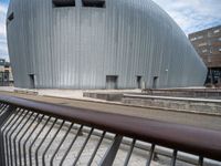 a long metal rail by the street near a building and a sidewalk with a sky background