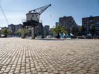 an open brick walkway leads to buildings near a crane tower in a city, and there is no traffic or any people