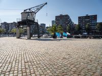 an open brick walkway leads to buildings near a crane tower in a city, and there is no traffic or any people