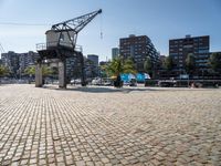 an open brick walkway leads to buildings near a crane tower in a city, and there is no traffic or any people