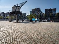 an open brick walkway leads to buildings near a crane tower in a city, and there is no traffic or any people