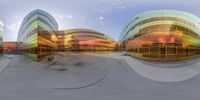 multiple curved glass walls surrounding a park in front of a building and clouds in the sky