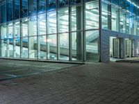 a building with windows reflecting it's lights at night, and a sidewalk at night