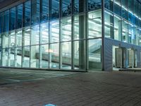 a building with windows reflecting it's lights at night, and a sidewalk at night