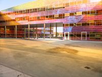 a parking lot with a brightly colored building on the other side of it, and a person riding an electric skateboard up the front door