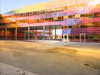 a parking lot with a brightly colored building on the other side of it, and a person riding an electric skateboard up the front door