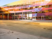 a parking lot with a brightly colored building on the other side of it, and a person riding an electric skateboard up the front door