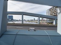 a metal bench sitting under an overpass next to a river view and a building