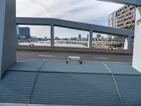 a metal bench sitting under an overpass next to a river view and a building