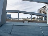 a metal bench sitting under an overpass next to a river view and a building