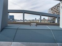 a metal bench sitting under an overpass next to a river view and a building