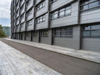 a building with a concrete sidewalk and windows on the side of it and a paved path between the buildings, which are empty