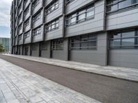 a building with a concrete sidewalk and windows on the side of it and a paved path between the buildings, which are empty