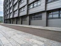 a building with a concrete sidewalk and windows on the side of it and a paved path between the buildings, which are empty