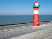 a person walking towards a lighthouse along the beach with a small animal nearby on the sand