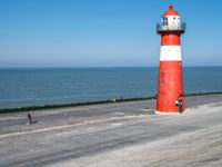 a person walking towards a lighthouse along the beach with a small animal nearby on the sand