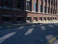 brick street in front of building with trees and buildings on it in shadow of the sun