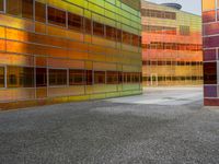 an abstractly colored building surrounded by a parking lot on asphalt, taken from the street