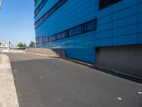 a skateboarder is going down the ramp by the street and blue building on a sunny day