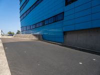 a skateboarder is going down the ramp by the street and blue building on a sunny day