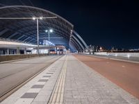 the road is empty and there are tracks going through it at night time, while people on benches line up to wait