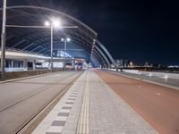 the road is empty and there are tracks going through it at night time, while people on benches line up to wait