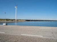 a person riding a skateboard by water near wind turbines at the shore of a lake