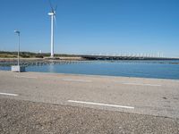 a person riding a skateboard by water near wind turbines at the shore of a lake