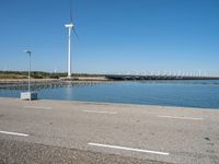 a person riding a skateboard by water near wind turbines at the shore of a lake