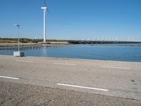 a person riding a skateboard by water near wind turbines at the shore of a lake