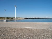 a person riding a skateboard by water near wind turbines at the shore of a lake