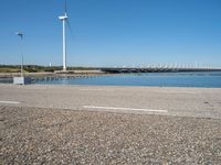 a person riding a skateboard by water near wind turbines at the shore of a lake