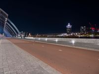 two people are riding their bicycle on a bridge next to the city at night with lights glowing from nearby buildings