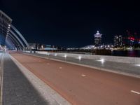 two people are riding their bicycle on a bridge next to the city at night with lights glowing from nearby buildings