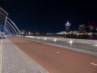 two people are riding their bicycle on a bridge next to the city at night with lights glowing from nearby buildings