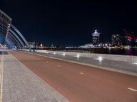 two people are riding their bicycle on a bridge next to the city at night with lights glowing from nearby buildings