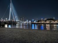 a view of the city skyline at night from across a river, with boats and bridge