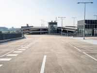 empty parking lot with large empty road and lights and building and fence to both sides