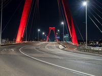 a large red bridge over a highway with lights in the background at night time, near an urban area