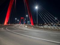 a large red bridge over a highway with lights in the background at night time, near an urban area