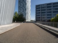 a long walkway runs near some buildings, a parking lot and the city beyond it