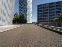 a long walkway runs near some buildings, a parking lot and the city beyond it