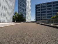 a long walkway runs near some buildings, a parking lot and the city beyond it